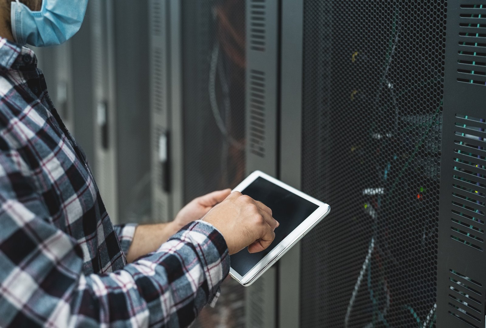 Male informatic engineer working inside server room database while wearing face mask